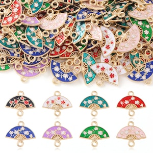 Może przedstawiać: Kolekcja kolorowych zawieszek w kształcie wachlarza ze złotymi metalowymi akcentami. Zawieszki mają kwiatowe wzory w różnych kolorach, w tym czerwonym, niebieskim, zielonym i różowym. Każda zawieszka ma dwie pętle do mocowania.