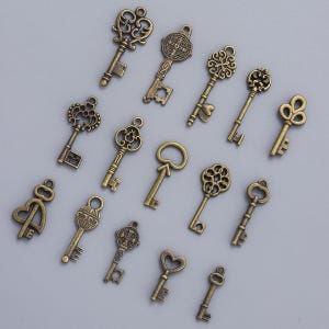 May include: An assortment of antique-style keys in various designs. The keys are made of a bronze-colored metal and feature ornate details, including floral patterns, hearts, and religious symbols. The keys are arranged on a light gray surface.