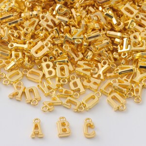 May include: A large pile of gold-colored metal letter charms, with the letters A, B, and C highlighted in the foreground.