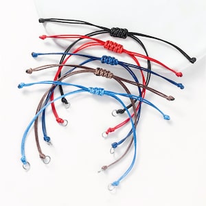 Puede incluir: Un conjunto de seis pulseras trenzadas de colores con cierres plateados. Las pulseras están hechas de diferentes colores de cuerda, incluyendo negro, rojo, azul, marrón y azul claro.