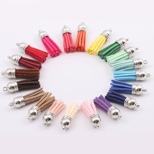 May include: Assortment of 20 colourful suede tassels with silver metal caps. The tassels are arranged in a circle on a white background.