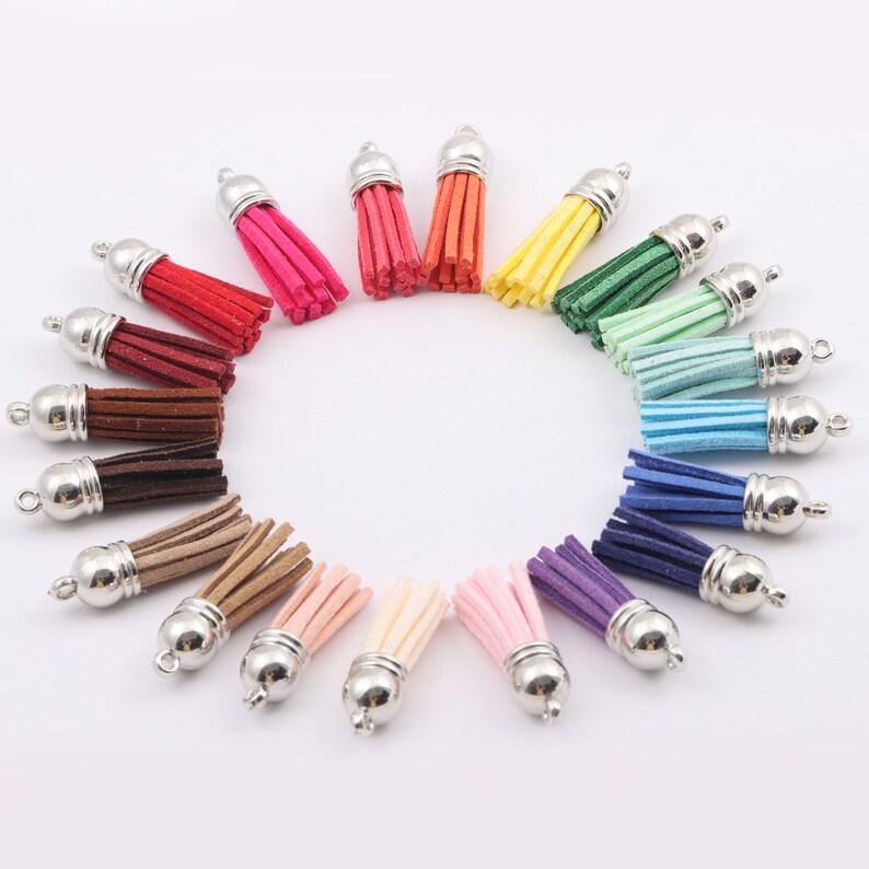 May include: Assortment of 20 colourful suede tassels with silver metal caps. The tassels are arranged in a circle on a white background.