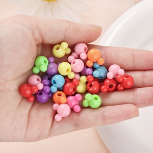 May include: A collection of colorful plastic beads in the shape of Mickey Mouse heads. The beads are in various colors, including red, orange, yellow, green, blue, purple, and pink.