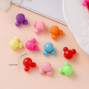 May include: Assortment of ten colorful plastic Mickey Mouse head shaped hair clips. The clips are approximately 1.16 inches in length and 0.8 inches in width. The colors include yellow, pink, red, blue, green, orange, and purple.