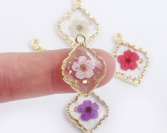 May include: Four gold-toned pendants with a diamond-shaped frame and a clear resin center. Each pendant features a different pressed flower in pink, white, red, and purple.