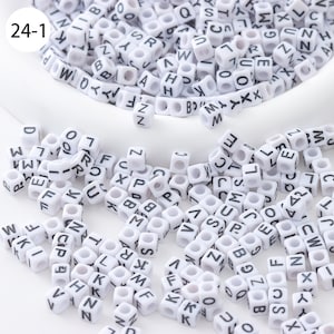 May include: A large quantity of white plastic letter beads with black lettering. The beads are scattered on a white surface. The beads are in a variety of letters, including A, B, C, D, E, F, G, H, I, J, K, L, M, N, O, P, Q, R, S, T, U, V, W, X, Y, and Z.