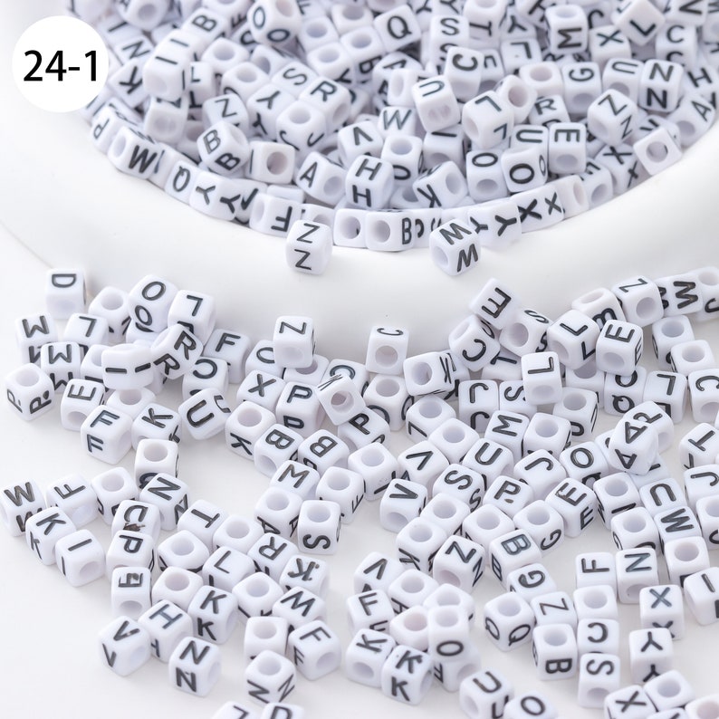 May include: A large quantity of white plastic letter beads with black lettering. The beads are scattered on a white surface. The beads are in a variety of letters, including A, B, C, D, E, F, G, H, I, J, K, L, M, N, O, P, Q, R, S, T, U, V, W, X, Y, and Z.