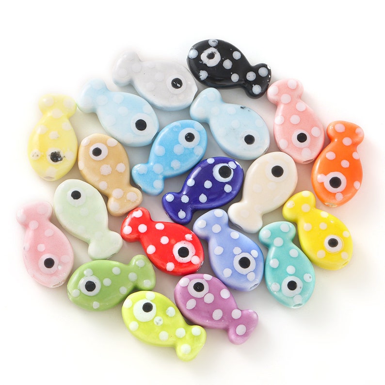 Pode incluir: Uma cole&ccedil;&atilde;o de contas de peixe de cer&acirc;mica coloridas com bolinhas brancas e olhos pretos. As contas est&atilde;o dispostas em c&iacute;rculo sobre um fundo branco.
