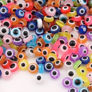 May include: A large assortment of colorful plastic evil eye beads. The beads are round with a raised eye design and come in a variety of colors, including blue, green, pink, yellow, orange, and purple.