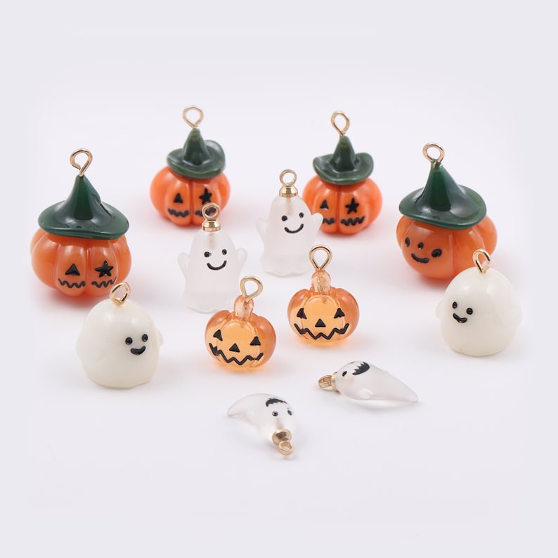Może przedstawiać: Kolekcja uroczych zawieszek na Halloween z motywem dyni i duch&oacute;w. Dynie są pomarańczowe z czarnymi twarzami jack-o'-lantern i zielonymi kapeluszami. Duchy są białe z czarnymi oczami i uśmiechami. Zawieszki mają złote k&oacute;łka do mocowania do biżuterii lub innych prac ręcznych.