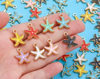 Pode incluir: Uma coleção de pingentes de estrela-do-mar coloridos com bordas douradas e laços para fazer joias. Os pingentes são em várias cores, incluindo amarelo, vermelho, azul, verde, rosa, branco, preto e roxo. O fundo é azul claro.