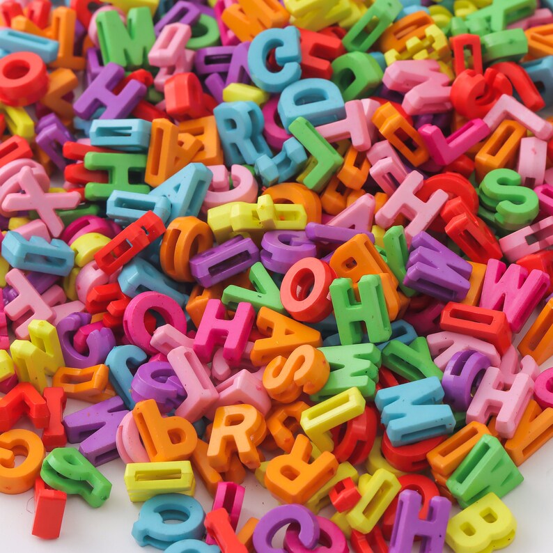 May include: A large pile of colorful plastic letter beads. The beads are in various colors, including red, orange, yellow, green, blue, purple, and pink. The beads are all in the shape of letters of the alphabet.