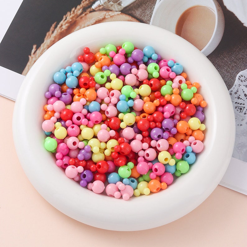 May include: A bowl filled with colorful plastic beads in various shapes, including round and Mickey Mouse-shaped beads. The beads are in shades of pink, purple, blue, green, yellow, orange, and red.