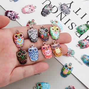 Pode incluir: Uma coleção de pingentes de coruja coloridos em vários designs. Os pingentes apresentam uma variedade de cores, incluindo vermelho, azul, verde e rosa. Cada pingente tem um pequeno laço na parte superior para prender a joias ou outros trabalhos manuais.