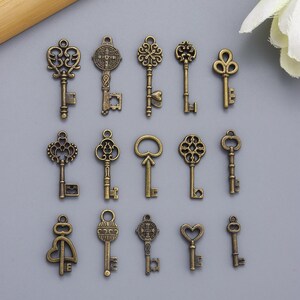 May include: A collection of antique-style keys in various designs. The keys are made of a bronze-colored metal and feature ornate details, including floral patterns, hearts, and religious symbols. The keys are arranged on a gray surface.