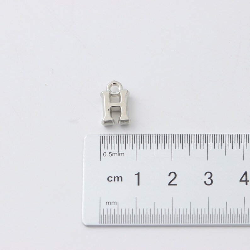May include: Silver charm in the shape of the letter H, measuring approximately 1 cm in height. The charm has a loop at the top for attaching to a bracelet or necklace.