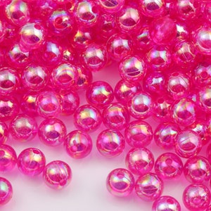 May include: A large pile of iridescent pink round beads. The beads are made of plastic and have a smooth, shiny finish.