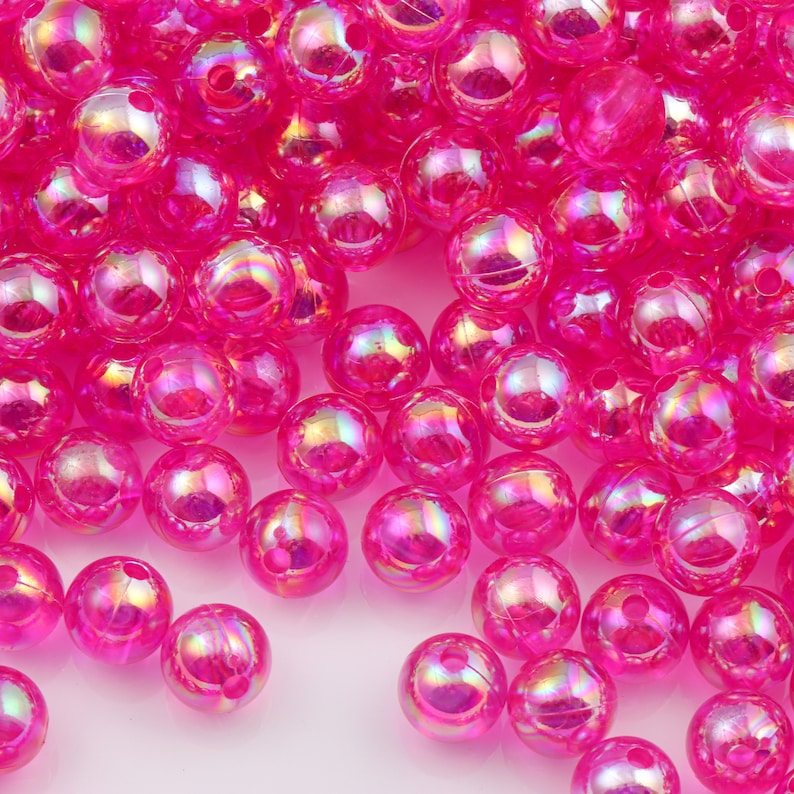 May include: A large pile of iridescent pink round beads. The beads are made of plastic and have a smooth, shiny finish.