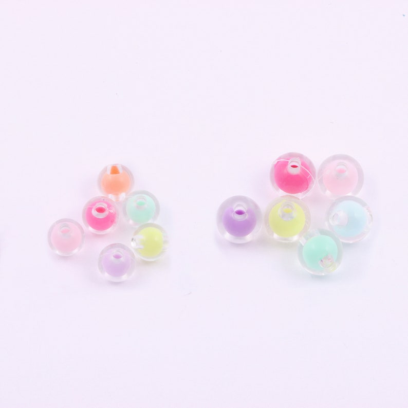 May include: A collection of colorful, translucent beads with pastel-colored centers. The beads are round with a hole through the center, and the colors include pink, purple, yellow, orange, and green. These beads are suitable for jewelry making and crafts.