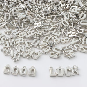 May include: A large pile of silver letter charms, with the words "GOOD LUCK" spelled out in larger charms at the bottom of the image.