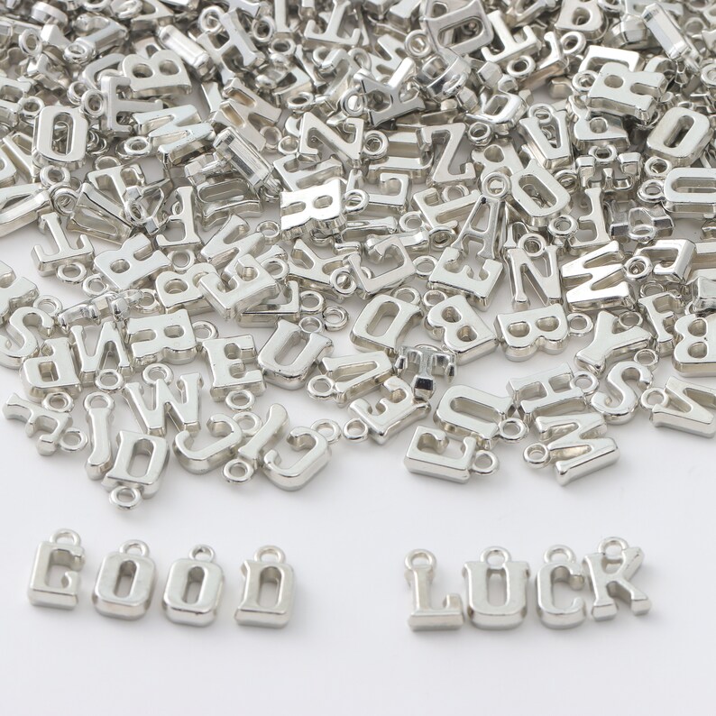 May include: A large pile of silver letter charms, with the words "GOOD LUCK" spelled out in larger charms at the bottom of the image.