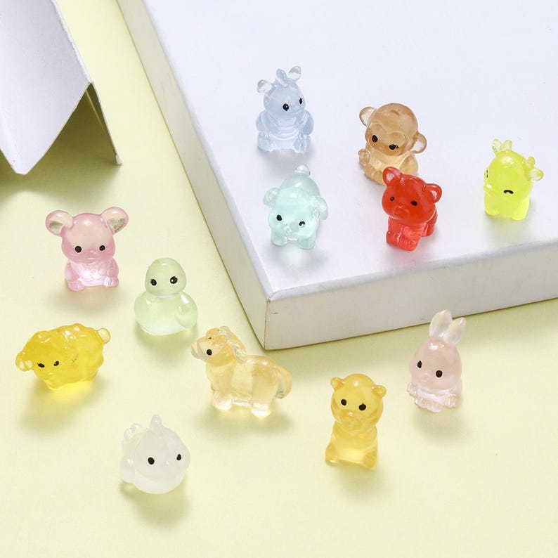 May include: A collection of small, translucent animal figurines in various colors, including pink, blue, yellow, and red. The figurines depict a bear, bunny, sheep, horse, and other animals. The figures are arranged on a white surface.