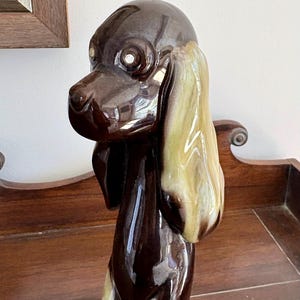 May include: A white ceramic mug with a black handle and the text "But First, Coffee" in a bold, black font. The mug is set against a blurred background, suggesting a cozy setting. The mug appears to be approximately 4 inches tall.