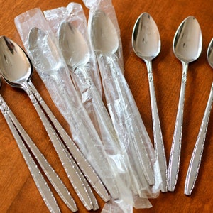 May include: A collection of six silver spoons, some still in their original packaging. The spoons have a decorative handle design and are displayed on a wooden surface.