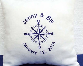 Könnte beinhalten: Ein weißes Kissen mit blauer Stickerei eines Kompasses und dem Text "Jenny & Bill January 12, 2015".