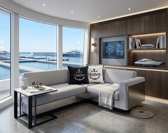 Könnte beinhalten: Ein hellgraues Ecksofa mit einem schwarzen Kissen mit Anker und dem Namen Charles sowie einem weißen Kissen mit Anker und dem Namen Elizabeth. Ein Beistelltisch mit weißer Platte und schwarzem Metallrahmen steht neben dem Sofa.