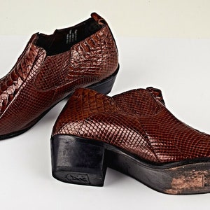 Könnte beinhalten: Ein Paar braune Lederstiefeletten mit Schlangenhautmuster. Die Stiefeletten haben eine spitze Zehenpartie und einen niedrigen Absatz.