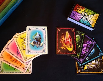 May include: A set of colorful playing cards with different crystal designs. The cards are laid out in a fan shape, with the top card showing a blue crystal with water droplets. The cards are surrounded by a black background.