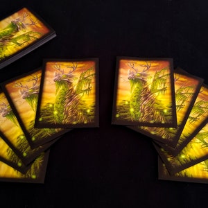 May include: A set of 10 cards featuring a green, deer-like creature with antlers, standing in a forest setting with a sunset background. The creature is surrounded by glowing green lights.