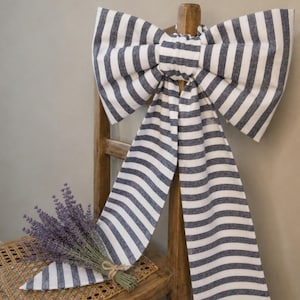 May include: A navy and white striped fabric bow adorns a wooden chair. A bunch of lavender, tied with twine, sits on the chair's woven seat. The scene evokes a sense of rustic charm and decorative elegance.