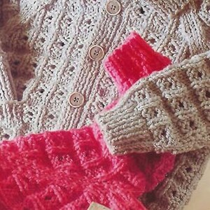 Puede incluir: Un cárdigan de punto con cuello y cierre de botones. El cárdigan es de color gris claro y tiene un delicado patrón de encaje. El cárdigan se superpone a un suéter de punto rosa.