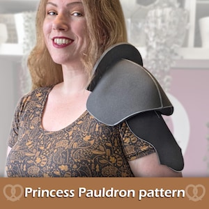May include: A dark gray foam pauldron worn on the shoulder, featuring a curved, layered design with smooth edges. The piece is constructed from a flexible material and sits over the shoulder area, displaying a solid matte finish throughout.