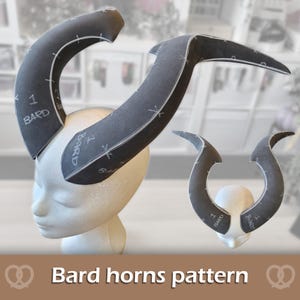 May include: A dark gray foam horn pattern for crafting, featuring white printed markings, numbers, and the text BARD. The pattern pieces are shown assembled on a white mannequin head, displaying curved, pointed shapes designed for headwear construction.