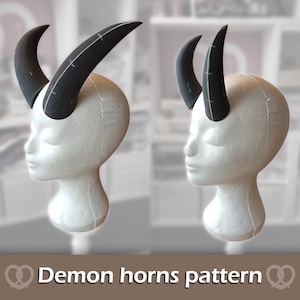 Könnte beinhalten: Zwei weiße Styropor-Mannequinköpfe mit schwarzen Dämonenhörnern. Die Hörner weisen sichtbare weiße Nahtlinien und Markierungen auf. Der Text "Demon horns pattern" ist in Weiß am unteren Bildrand gedruckt und von Brezel-Symbolen umrahmt.