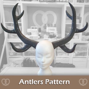 May include: A pair of dark gray, curved antlers attached to a white mannequin head. The antlers have white markings and are labeled with numbers. The text "Antlers Pattern" is displayed at the bottom of the image.