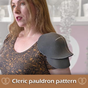 Könnte beinhalten: Ein dunkelgraues, geschwungenes Schulterstück mit sichtbaren weißen Nahtlinien, getragen über einem braunen kurzärmeligen Shirt mit Waldmuster. Der Text "Cleric pauldron pattern" ist am unteren Bildrand zu sehen.