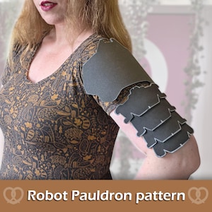 May include: A dark gray, multi-layered robot pauldron armor piece worn on the upper arm. The armor features a large shoulder plate followed by four smaller, overlapping articulated segments with light gray edges. Text reads: Robot Pauldron pattern.