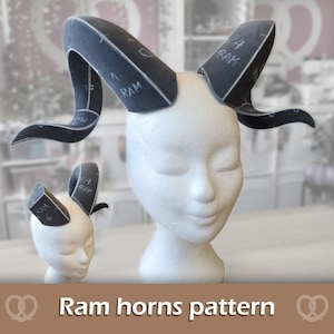 May include: A set of dark grey foam ram horns with white printed assembly markings and the text RAM 4, displayed on two white mannequin heads. The horns feature curved, pointed shapes and visible seam lines for construction and crafting.