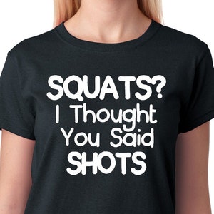 May include: Black t-shirt with white text that reads "SQUATS? I Thought You Said SHOTS"