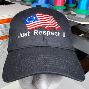 May include: A black baseball cap with an embroidered American flag and the text "Just Respect It".
