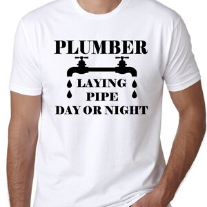 May include: White t-shirt with black text that reads "Plumber Laying Pipe Day or Night" with a graphic of two water faucets with water drops.