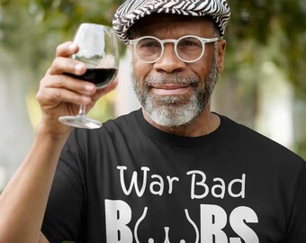 May include: Black t-shirt with the text "War Bad Boobs Good" in white. The image shows a person wearing a black and white patterned cap and glasses, holding a glass of red wine.