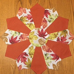 May include: A round table runner with a white background and a pattern of colorful autumn leaves. The runner is made of fabric and has a red and white polka dot border.