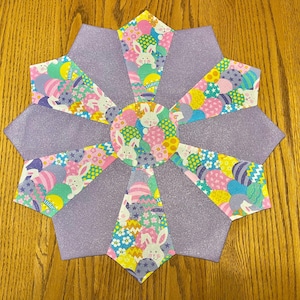 May include: A purple and white fabric table runner with a starburst design. The fabric features a pattern of pastel colored eggs and bunnies.
