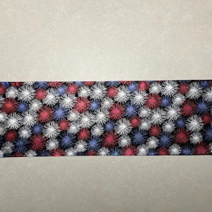May include: A decorative table runner with a repeating pattern of red, white, and blue starbursts on a black background. The runner has a pointed end and is likely made of fabric.