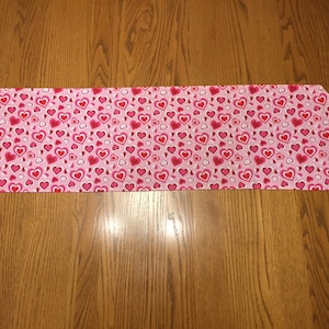 May include: A pink table runner with a pattern of red and white hearts.